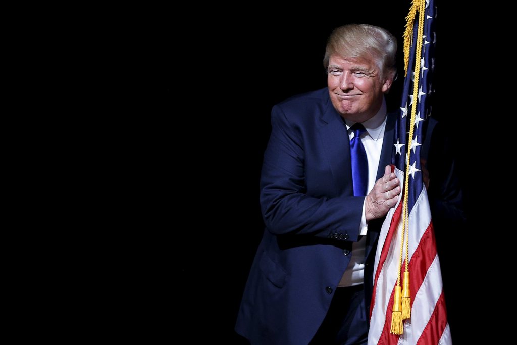 Image: U.S. Republican presidential candidate Trump hugs a U.S. flag as he takes the stage for a campaign town hall meeting in Derry